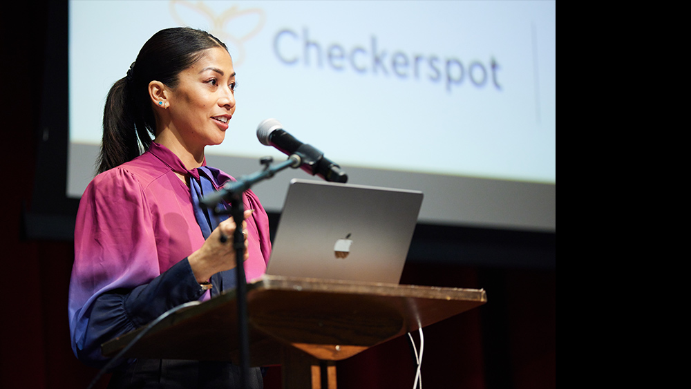 Nina Reyes stands at a podium speaking. Photo courtesy of Nina Reyes.