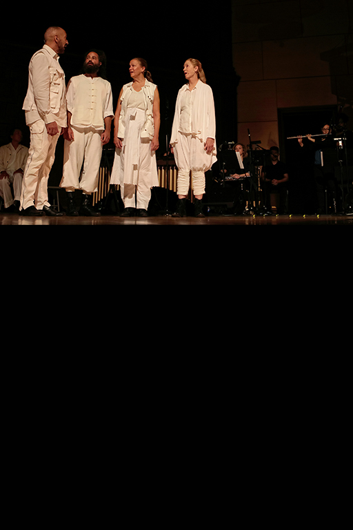 Four singers dressed in white stand in a line on stage, with a flute player to their side. Phot by Yvonne Portra.
