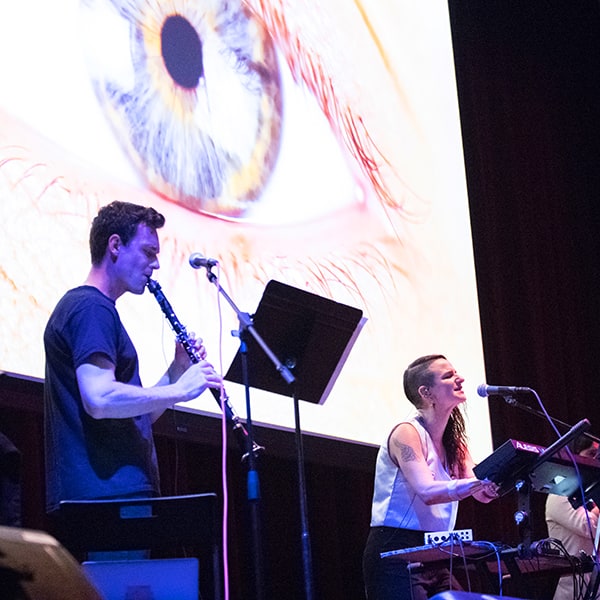 A clarinet player and keyboardist perform a multimedia piece before a projection screen at a Mills Music Now concert in Oakland, California.