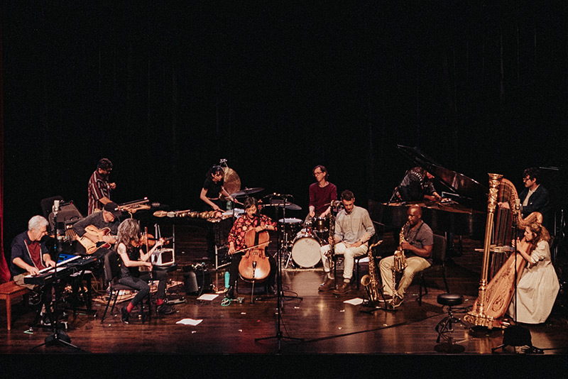 An improvisational ensemble of including keyboards, harp, violin, cello, drum set, saxophone are arrayed across a stage for a Mills Music Now concert in Oakland, California. Photo by Robbie Sweeny