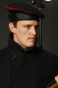 Stormy Henry Knight in a three quarter profile, dressed in  a black uniform of coat and beret hat with red trim. Photo courtesy of the artist.