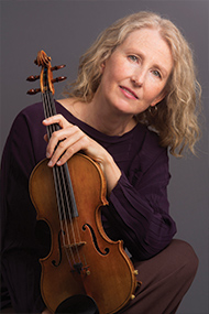 Violinist Kate Stenberg is prohographed with their violin in a studio, crouching with the instrument held infront of the body. Photo courtesy of the artist.